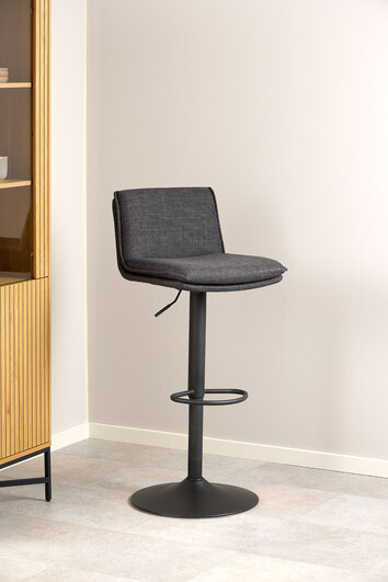 Flynn Barstol i stoffet Basel Mørkegrå som står mod en beige væg