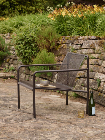 Dapple Loungestol i farven Dark Chocolate, som står på en stenbelagt udeplads fyldt med blomster og grønt