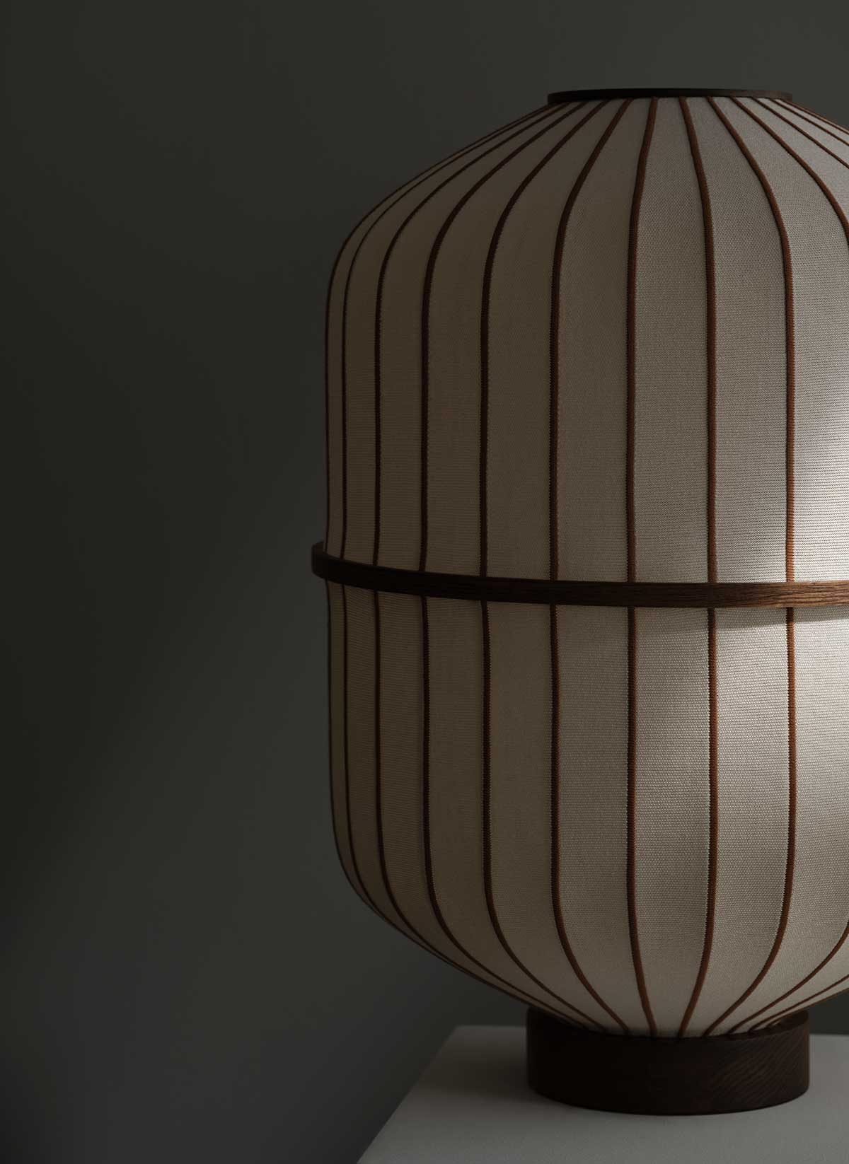 Bolia-Lucen-Table-Lamp-Sand-Dark-Oiled-Oak-Lifestyle-1.jpg Lucén bordlampe i mørkolieret eg i et dæmpet rum, hvor en stribe lys skinner ind.