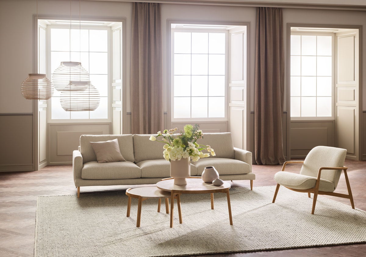 Veneda sofa 4-personers i et lyst stof i en stue med smukt lysindfald og moderne møbler.
