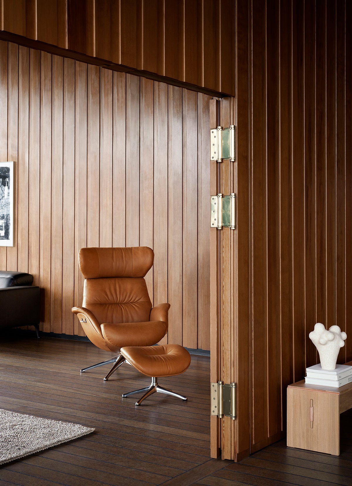 More Lænestol og fodskammel i læderet Dakota Modern Cognac Brown med ben i poleret aluminium i et rum beklædt med træpaneler