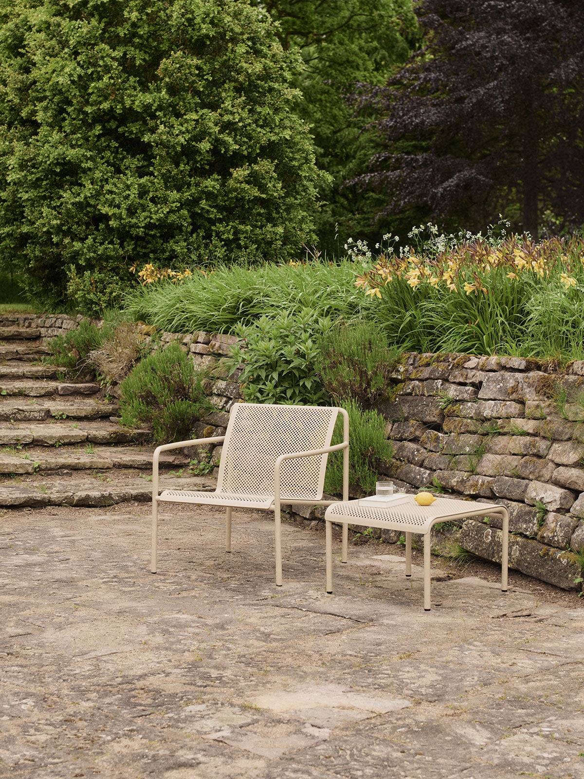 Dapple Loungestol og Dapple Loungebord 57x57 i farven Cashmere, som står på en stenbelagt udeplads