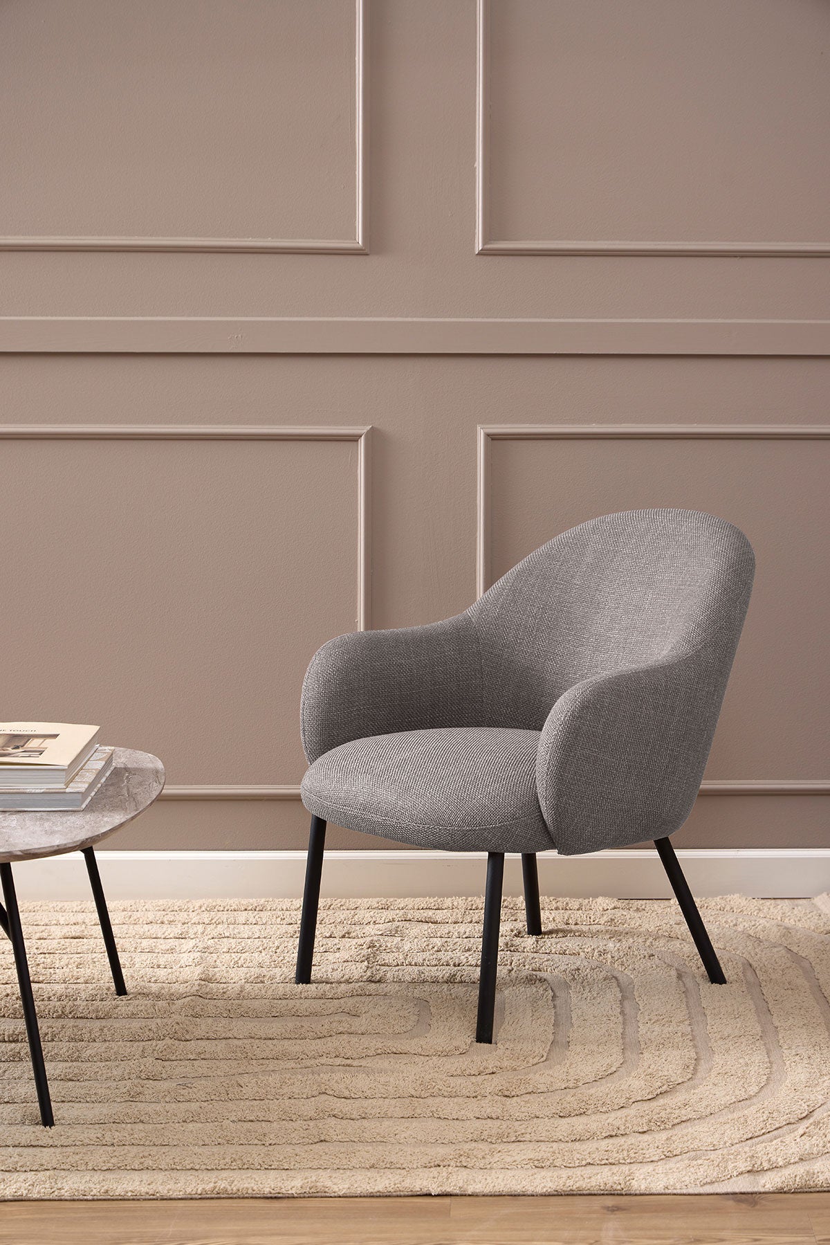 Spencer Loungestol i stoffet Basel Lysegråbrun som står på et beige uldtæppe