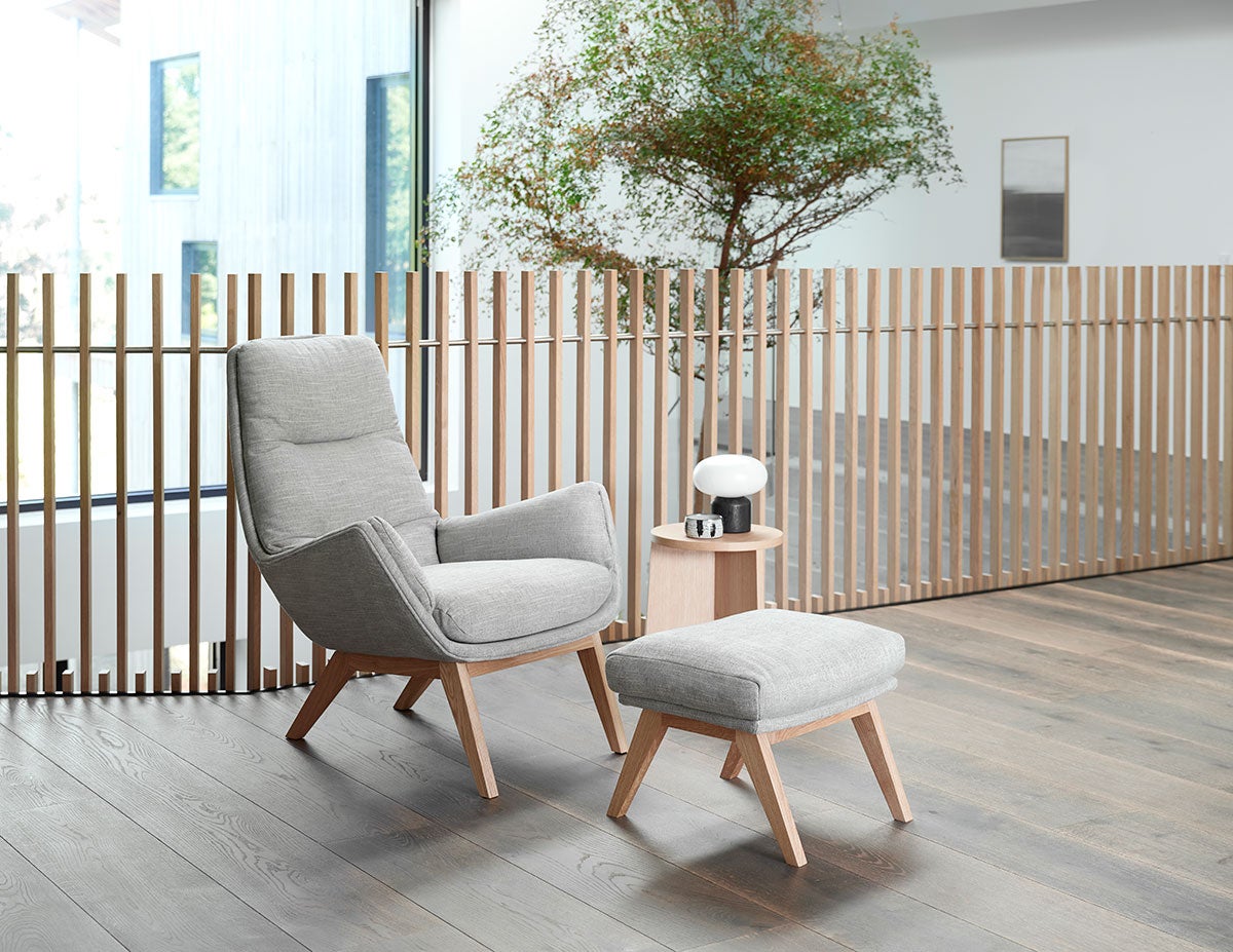 Moro Lænestol og fodskammel i stoffet Brescia Calm Grey med ben i eg i et lyst kontormiljø