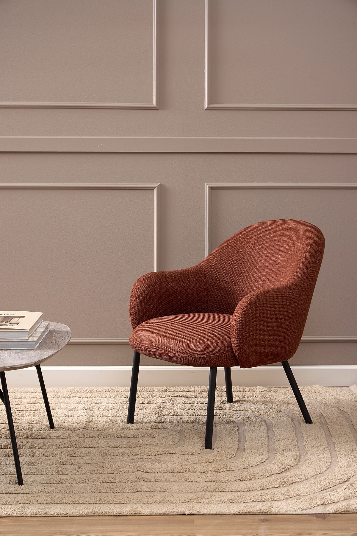 Spencer Loungestol i stoffet Basel Terrakotta som står på et beige uldtæppe