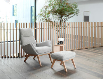 Moro Lænestol og fodskammel i stoffet Brescia Calm Grey med ben i eg i et lyst kontormiljø