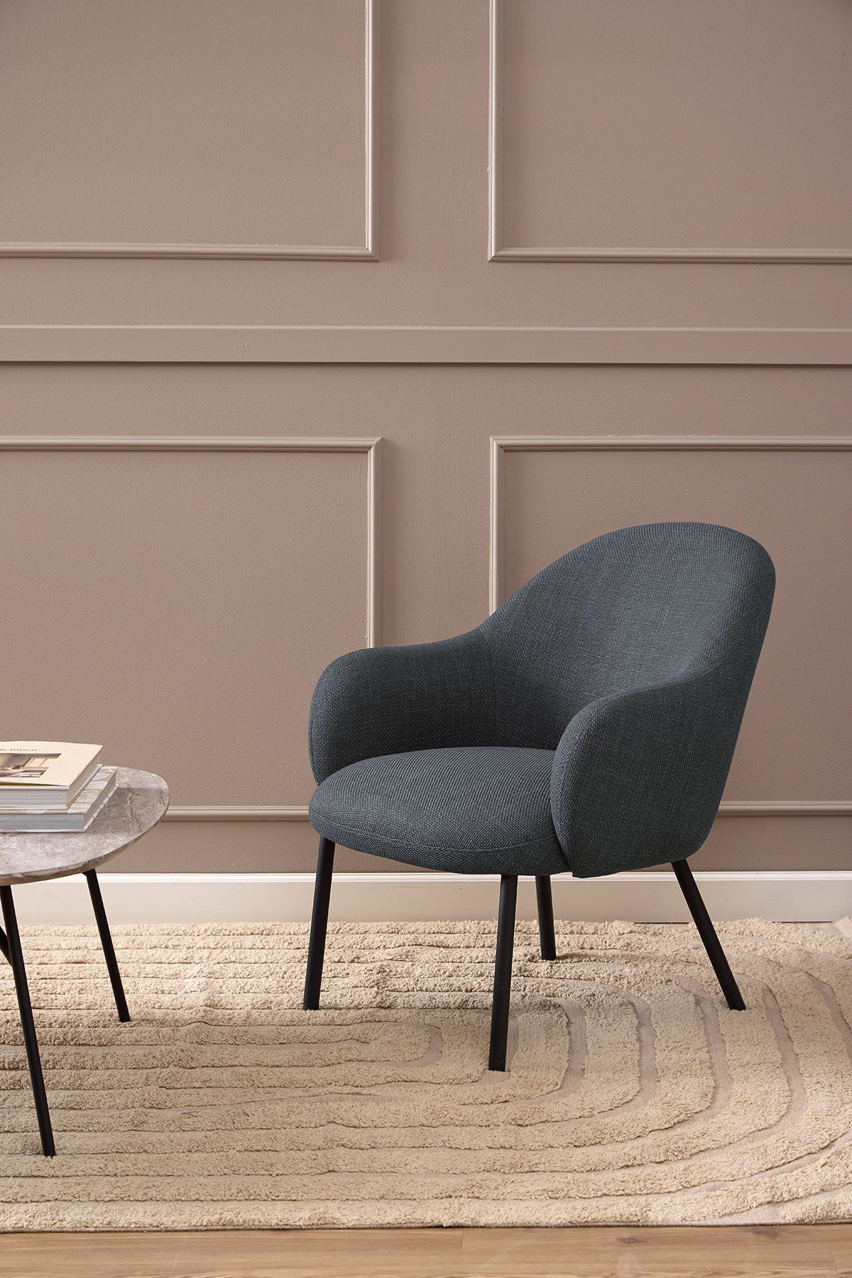 Spencer Loungestol i stoffet Basel Mørkegrå som står på et beige uldtæppe