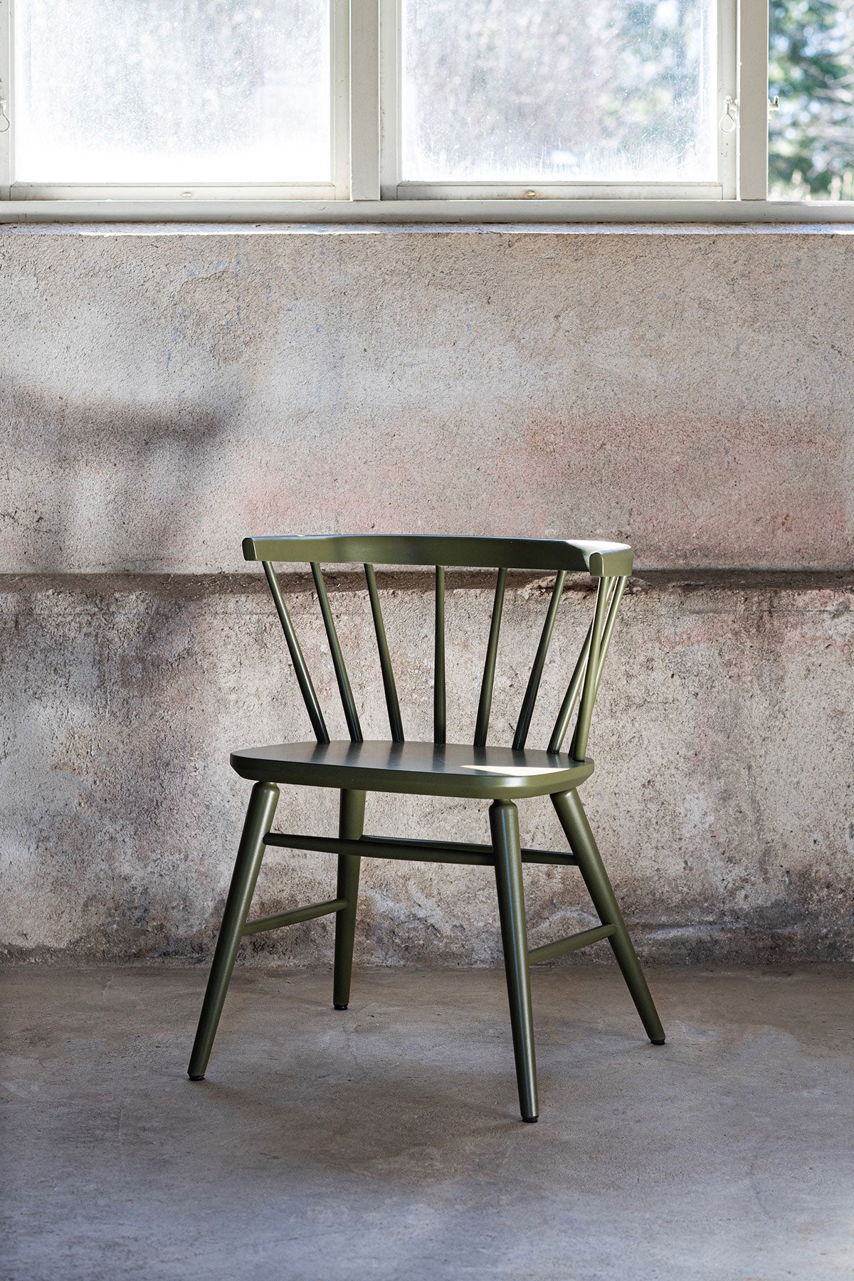 Florida Armstol i Wigellsgrøn lak i et rum med rå betonvæg og et vindue, der lukker dagslys ind