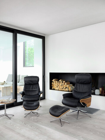 Aarhus Lænestol og fodskammel med finérsider i læderet Savoy i farven Platin Black foran brændeopbevaring