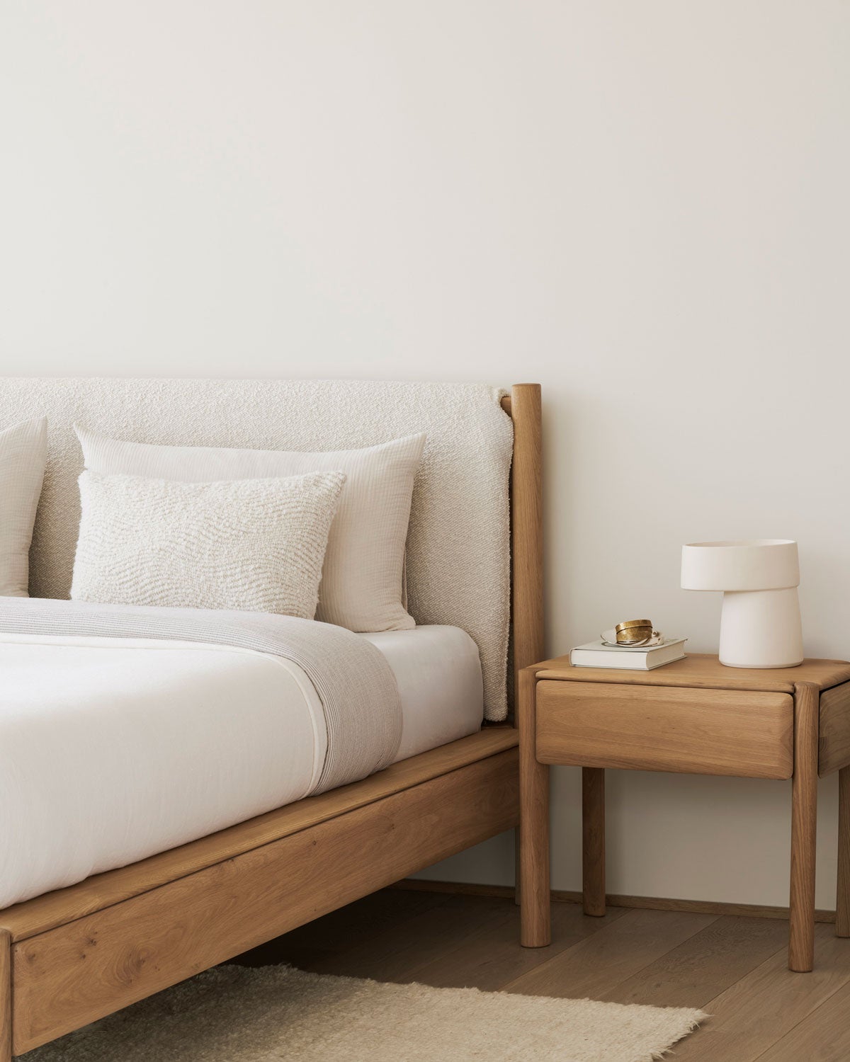PI Sengeramme 160x200 i stoffet Cloud i et soveværelse med et sengebord. Sengen er redt med hvidt sengetøj.