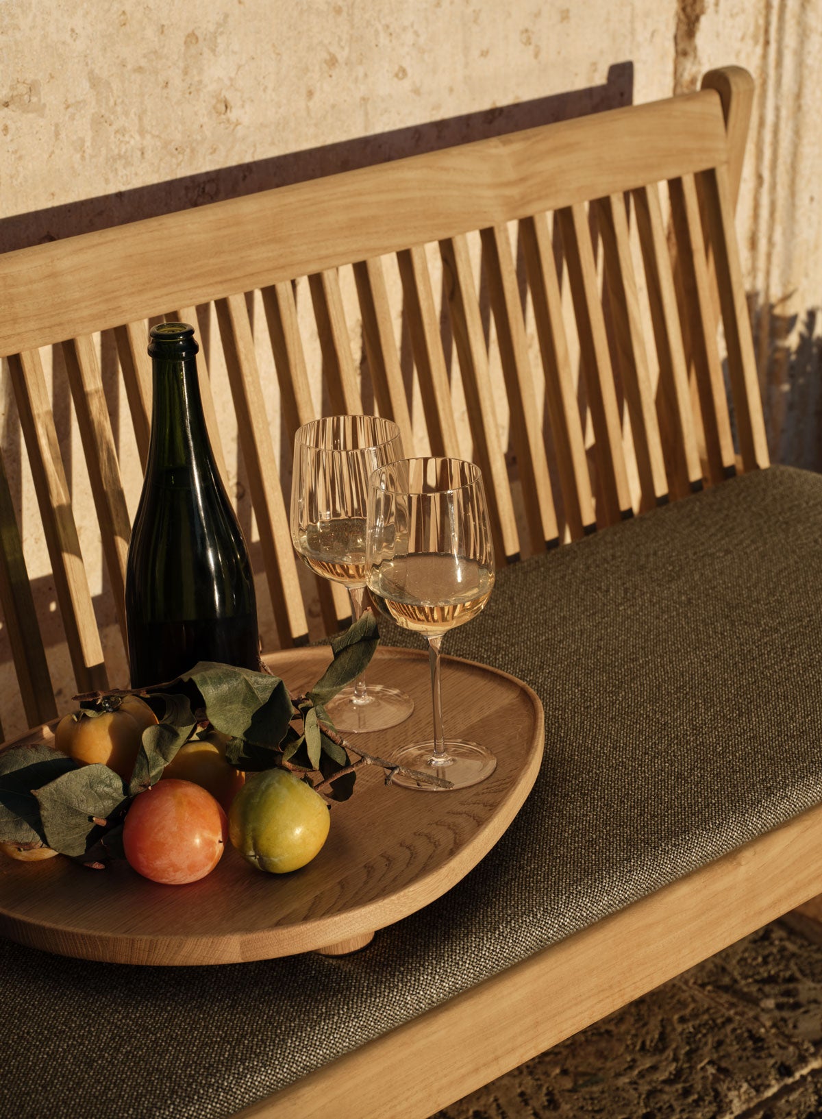 Patio havebænk i solnedgang med en bakke med citrusfrugter, en flaske vin og to halvt fyldte vinglas.