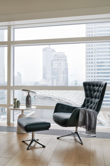 Sini Lænestol og fodskammel i læderet Savoy Deep Forest Green med ben i poleret aluminium foran et vindue med udsigt til skyskrabere