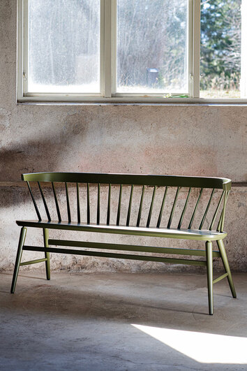 Florida Pindebænk i Wigellsgrøn lak i et rum med rå betonvæg og et vindue, der lukker dagslys ind