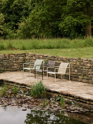 Dapple Loungestol i farverne Tea Green, Dark Chocolate og Cashmere, som står på række ved siden af en dam