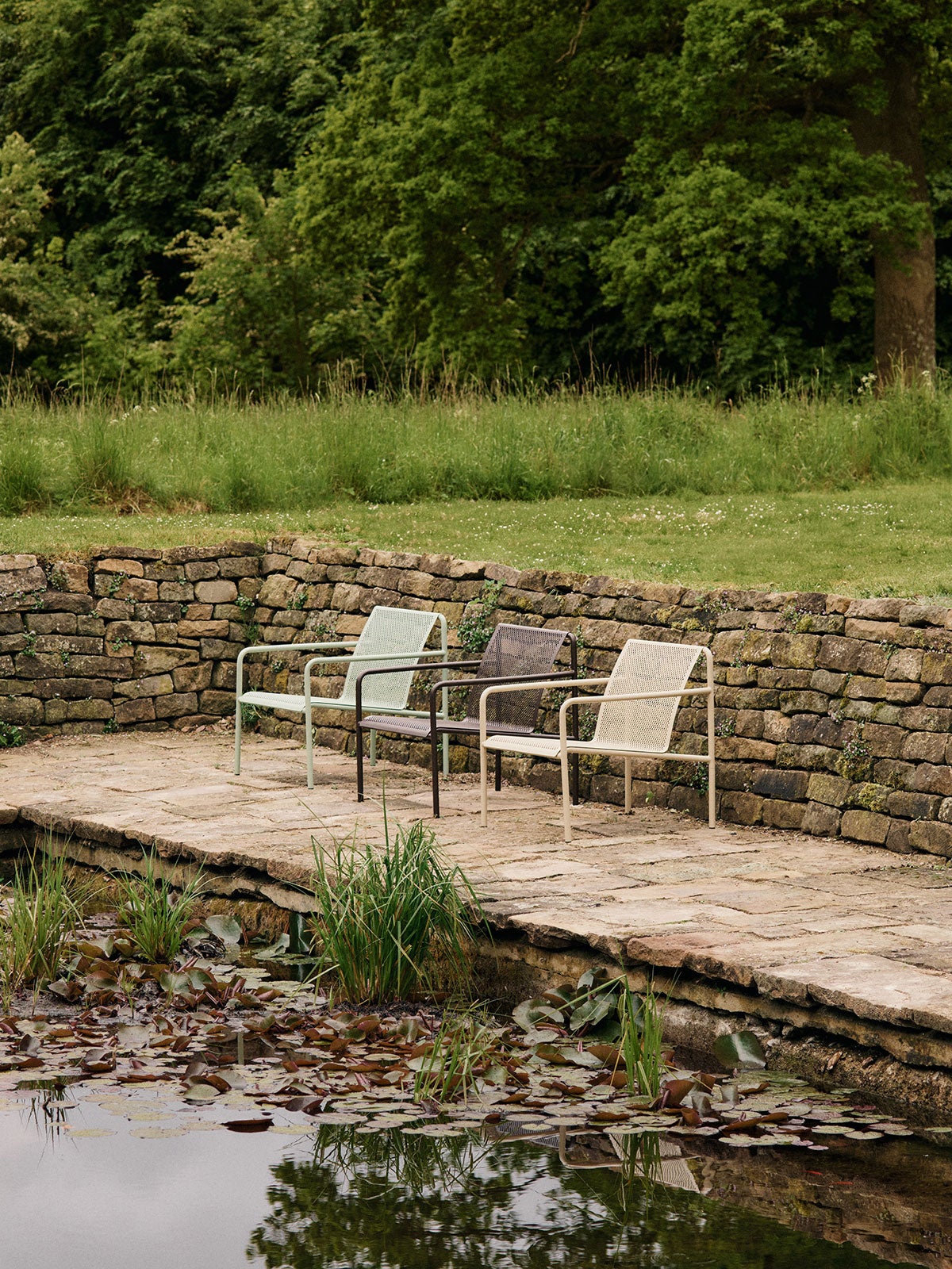 Dapple Loungestol i farverne Tea Green, Dark Chocolate og Cashmere, som står på række ved siden af en dam